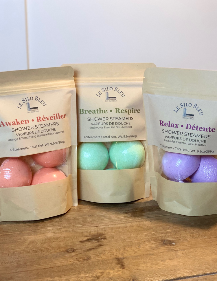 Collection of Shower Steamers, three types, Orange, Eucalyptus and Lavender. Three bags sitting on a wooden tabletop with a white background.