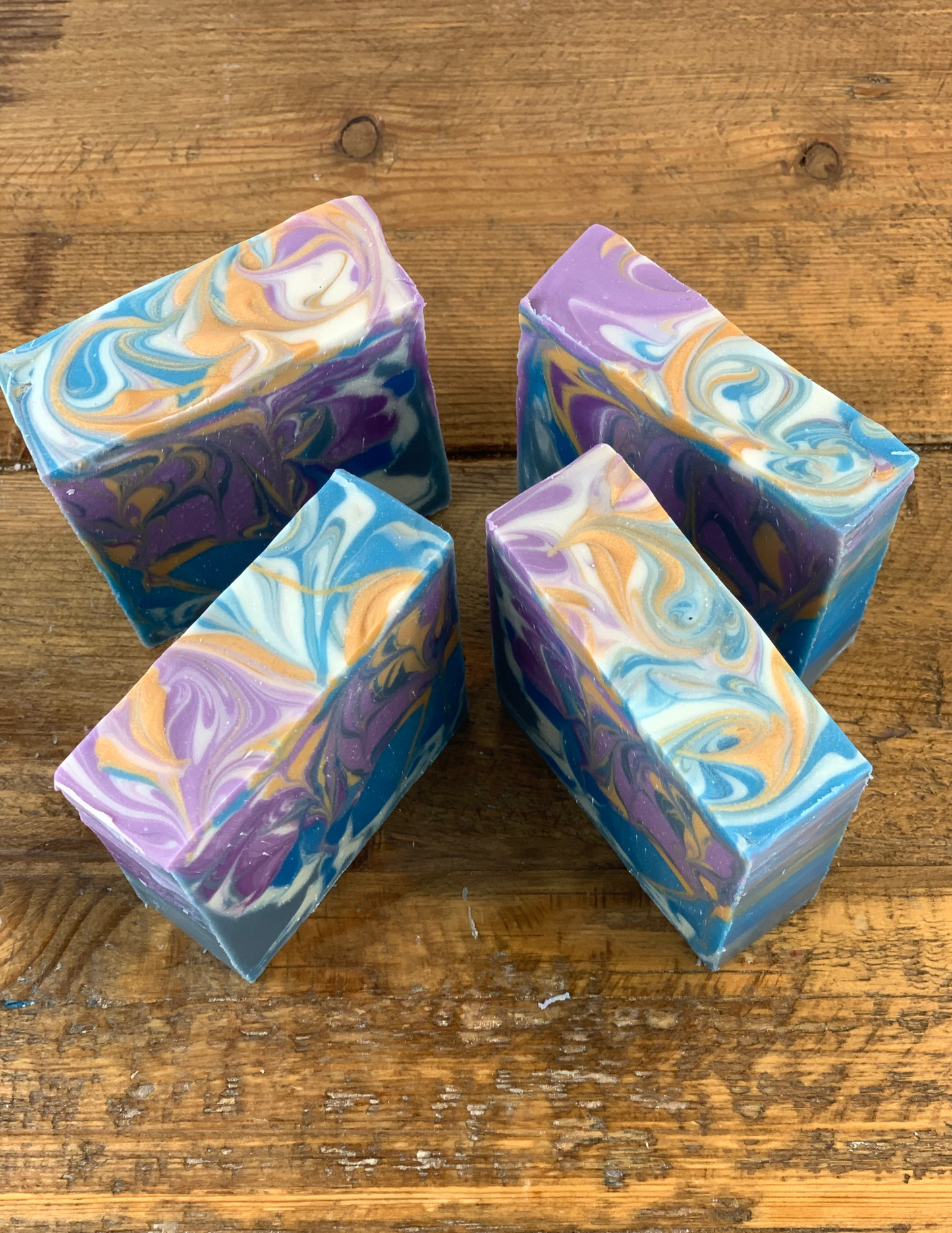 Four bars showing their swirled tops in purple, blue, gold and white swirls. Bars are sitting on a wooden table. 