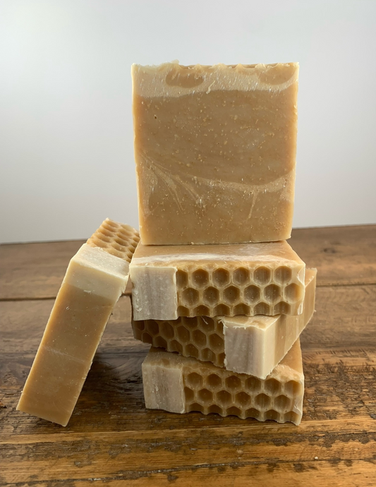 Stack of Triple Butter Honey Soap on a wooden table with a white background. Another bar of soap leans against the stack.