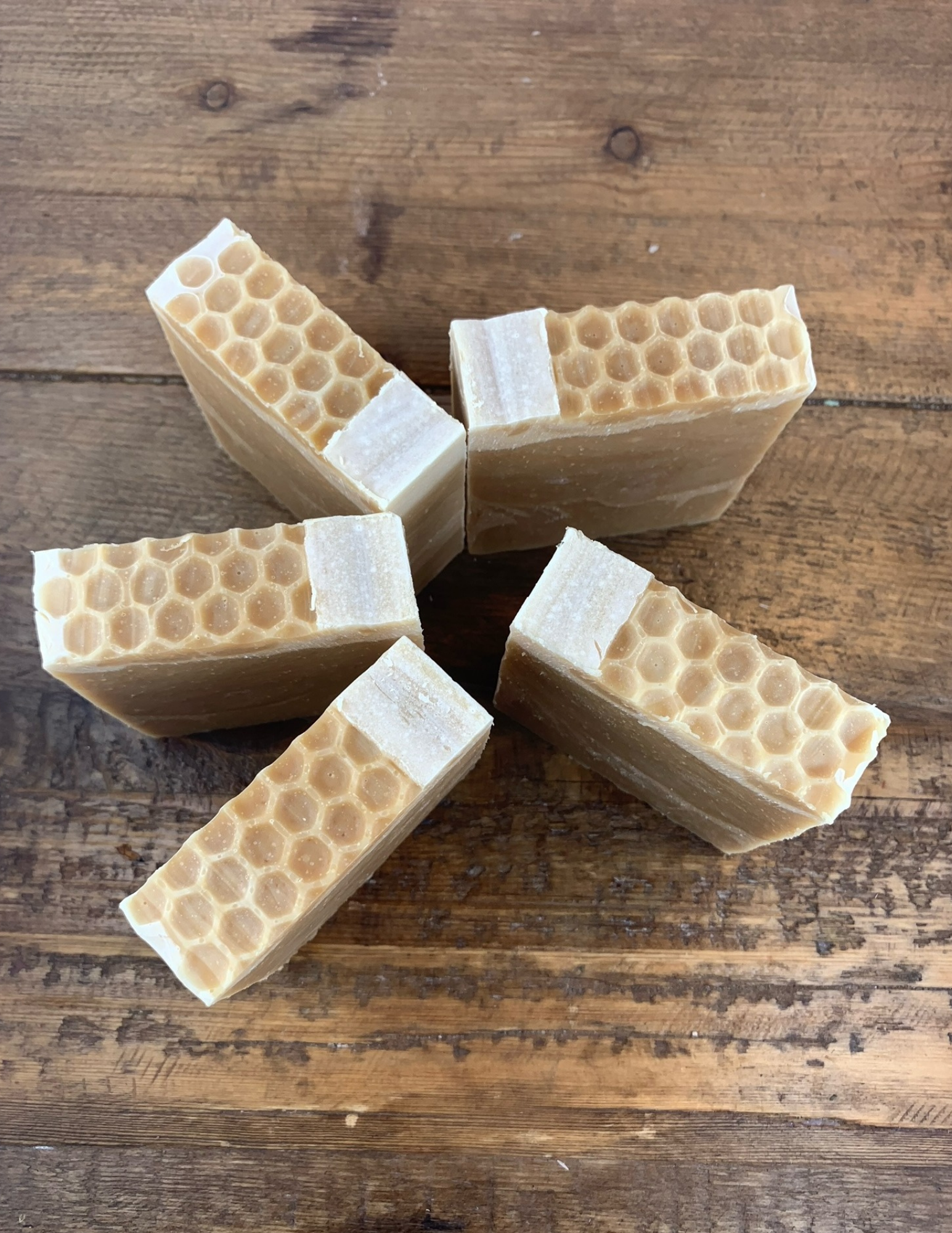 Five bars of Triple Butter Honey Soap sit on a wooden table. Detailing shows the honeycomb tops of the soaps.