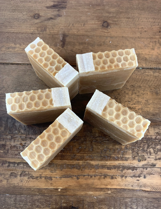 Five bars of Triple Butter Honey Soap sit on a wooden table. Detailing shows the honeycomb tops of the soaps.