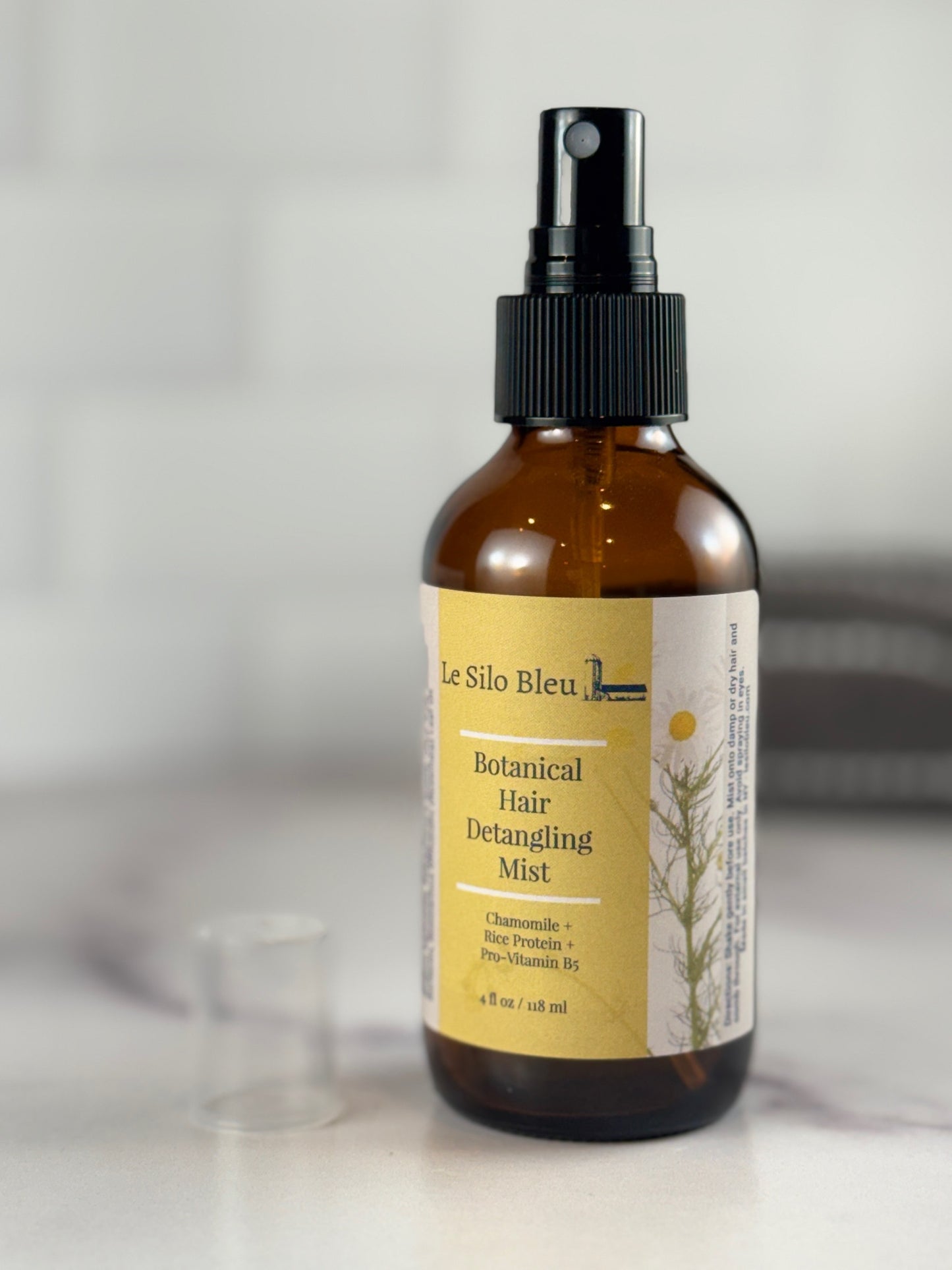 Brown spray bottle with a yellow label on a light background for the detangling mist made with chamomile rice protein and vit. b5