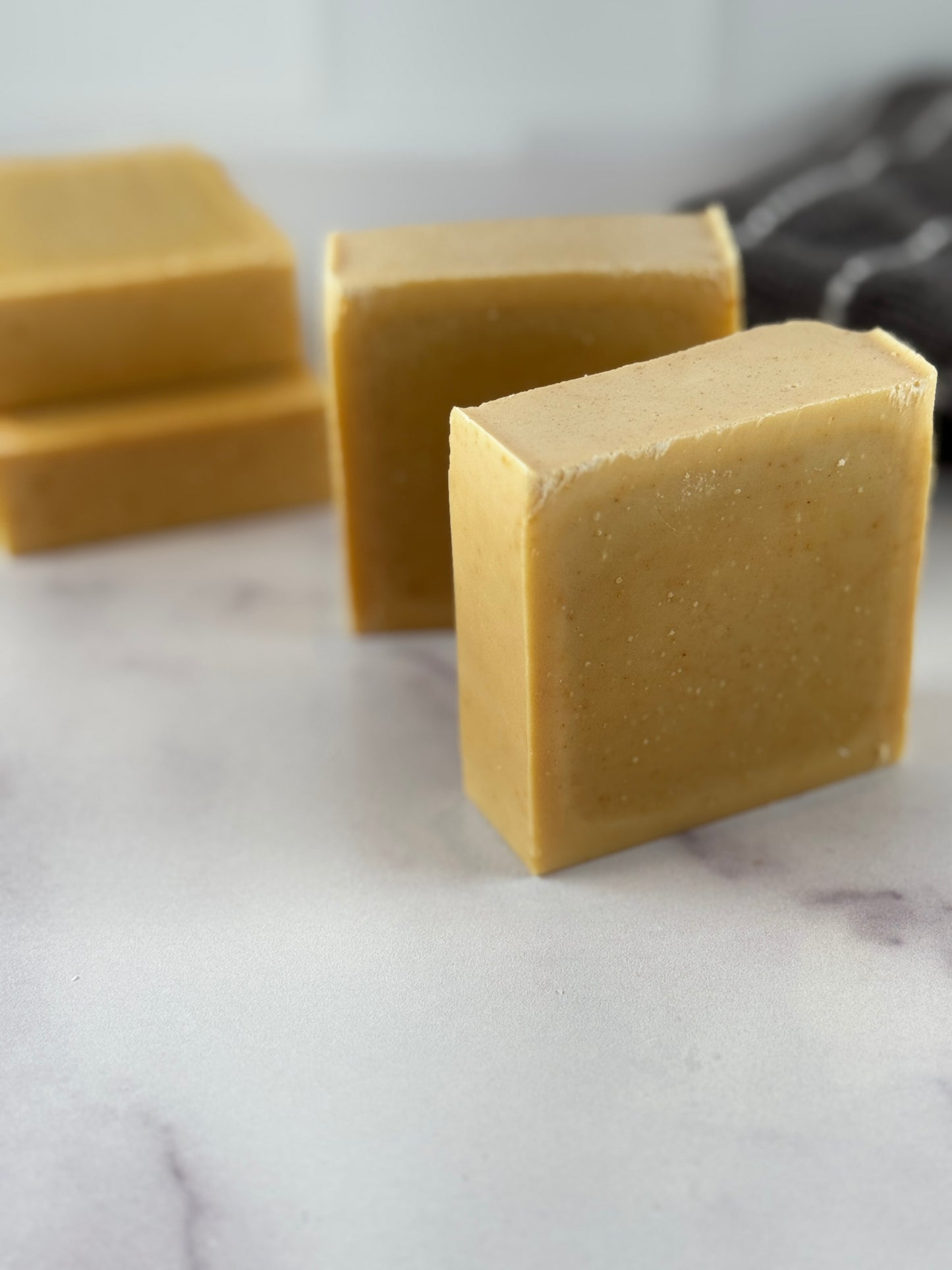 Three bars of natural turmeric soap in a warm tan color, arranged on a white marble surface with a soft-focus background.