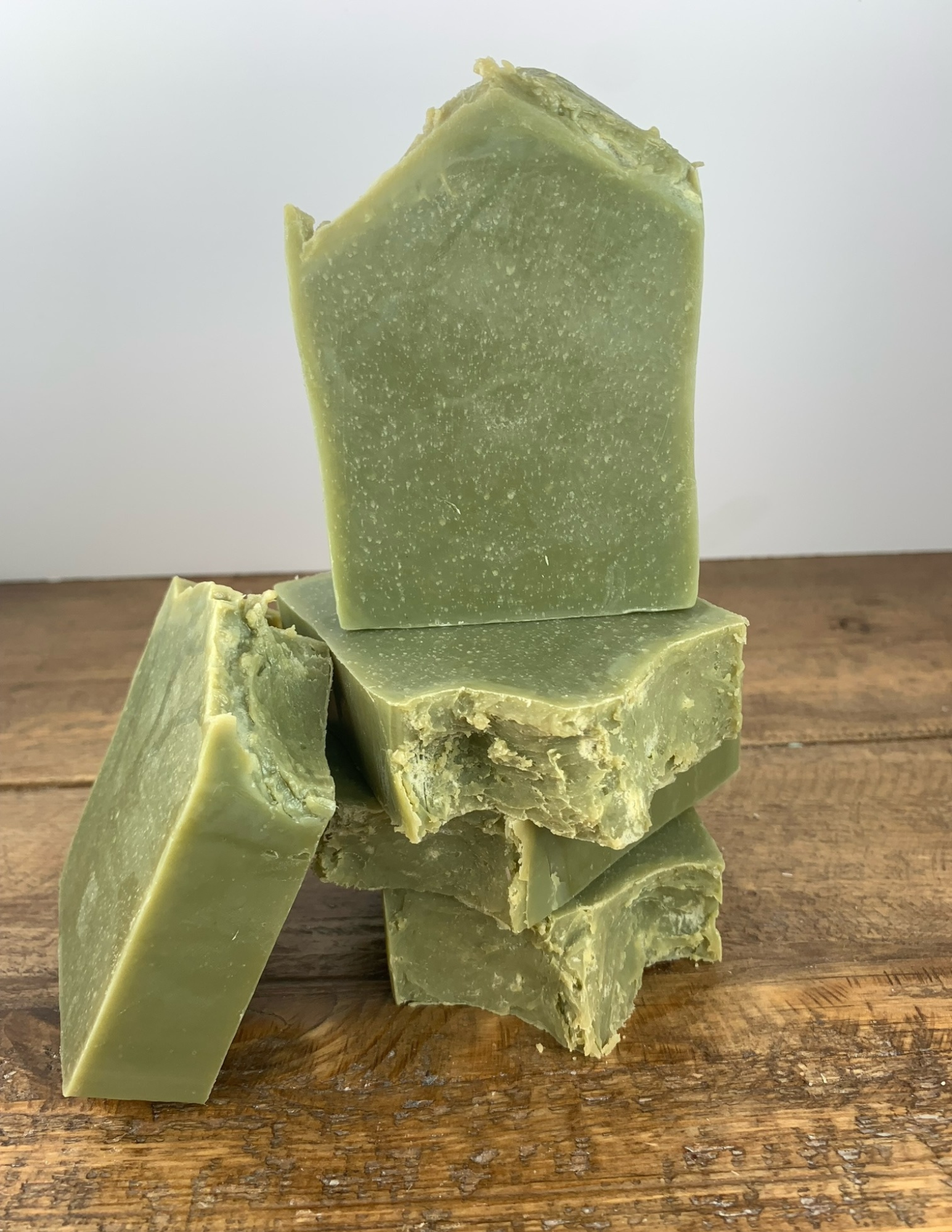 Four bars of this refreshing spearmint scented soap sit atop a wooden table. This soap is a dark green from the spurlina powder and features essential oils.