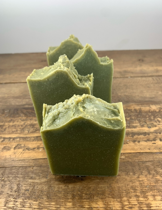 Four bars of this refreshing spearmint scented soap sit in a line atop a wooden table. This soap is a dark green from the spurlina powder and features essential oils. 