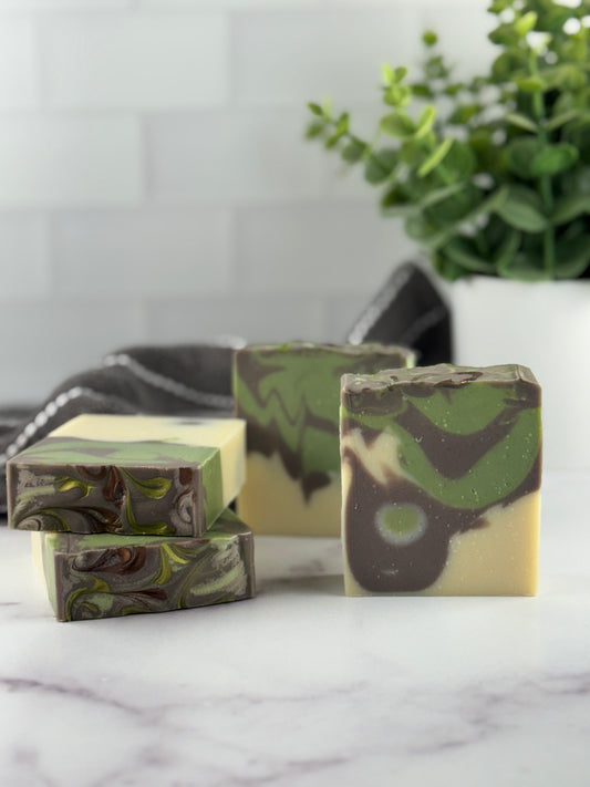 Green and brown marbled soap bars on a marble surface with a plant in the background