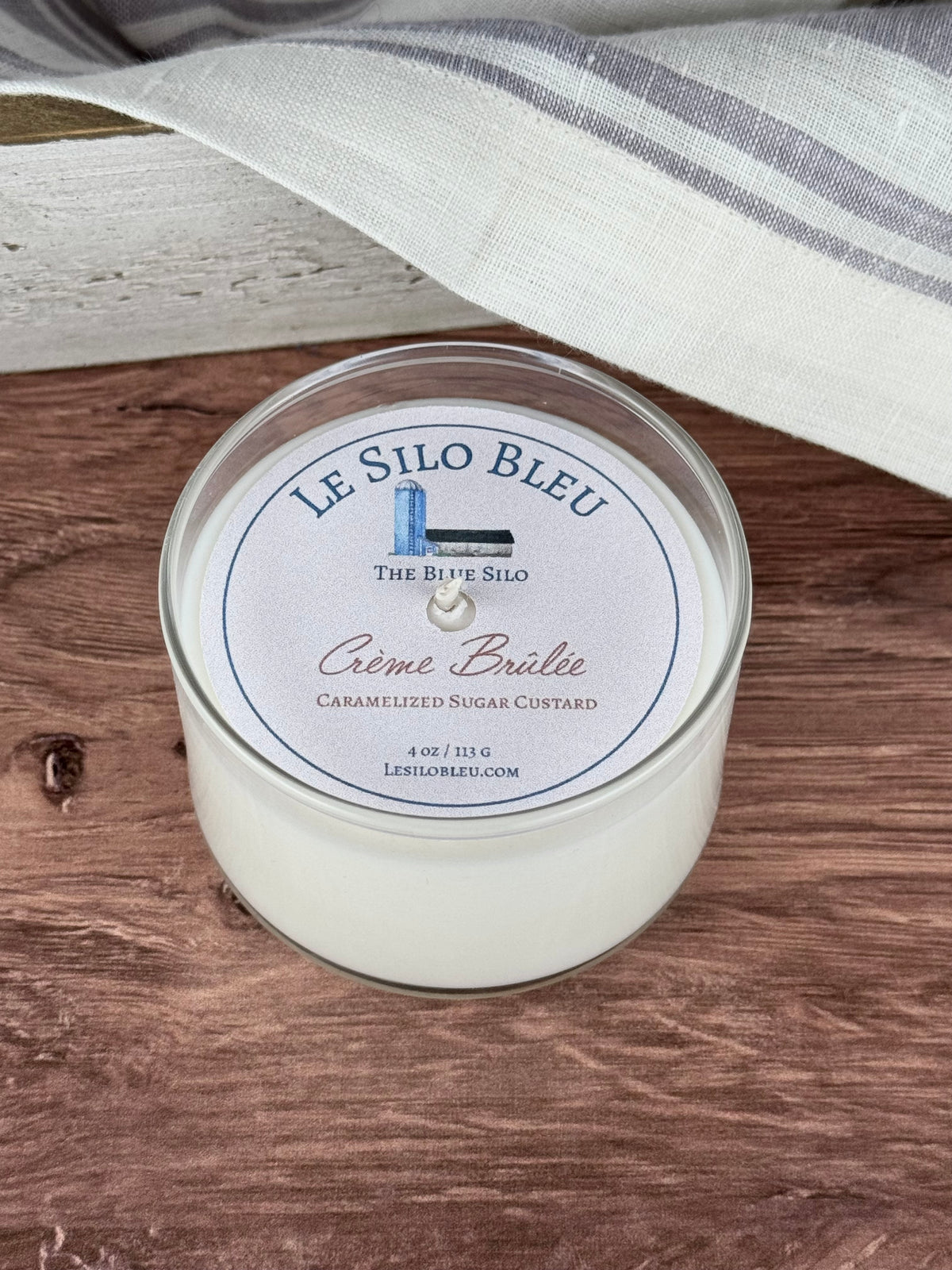 Small scented soy wax candle with label 'LE SILON BLEU' and 'CÉme Brülée Caramelized Sugar Custard' on a wooden table.