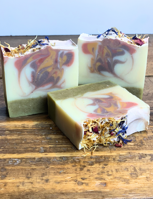 Three Spring Meadow soaps sitting on a wood tabletop with floral botanical petals on top.