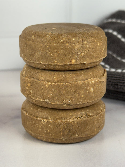Stack of Nourishing Solid Shampoo bars on a white surface with a black and white striped towel in the background.
