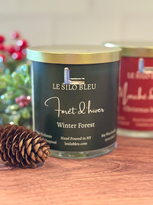 Le Silo Bleu candle labeled 'Winter Forest' with a pine cone on a wooden surface.