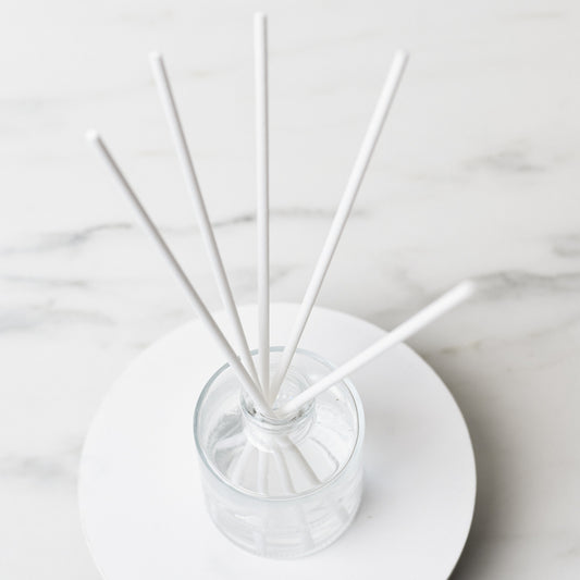 White reeds in a bottle on a white top on a white marble table.
