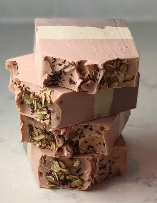 This handcrafted cold-processed soap is made with oat milk and natural clays. This lovely, oat-scented bar is extra creamy and produces a nice lather. A stack of four of these three color bars sits on a marble counter. Made with Brazilian Purple Clay and Rose Clay for a pretty striped effect. Topped with Oats and Heather flowers. 