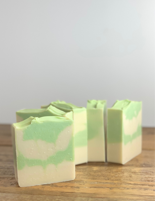 Bars of Eucalyptus Mint soap on a wooden tabletop with a white background. the soap is white with green swirls and green top.