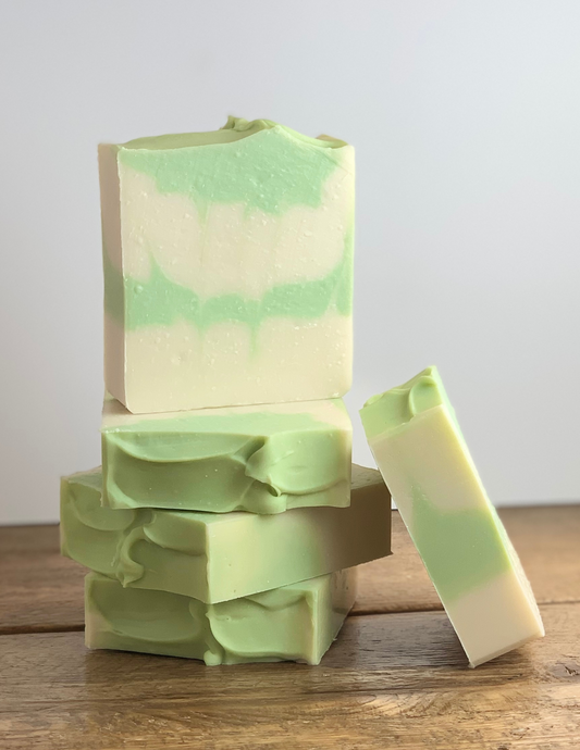 Stack of Eucalyptus Mint soap on a wooden tabletop with a white background. the soap is white with green swirls and green top. 