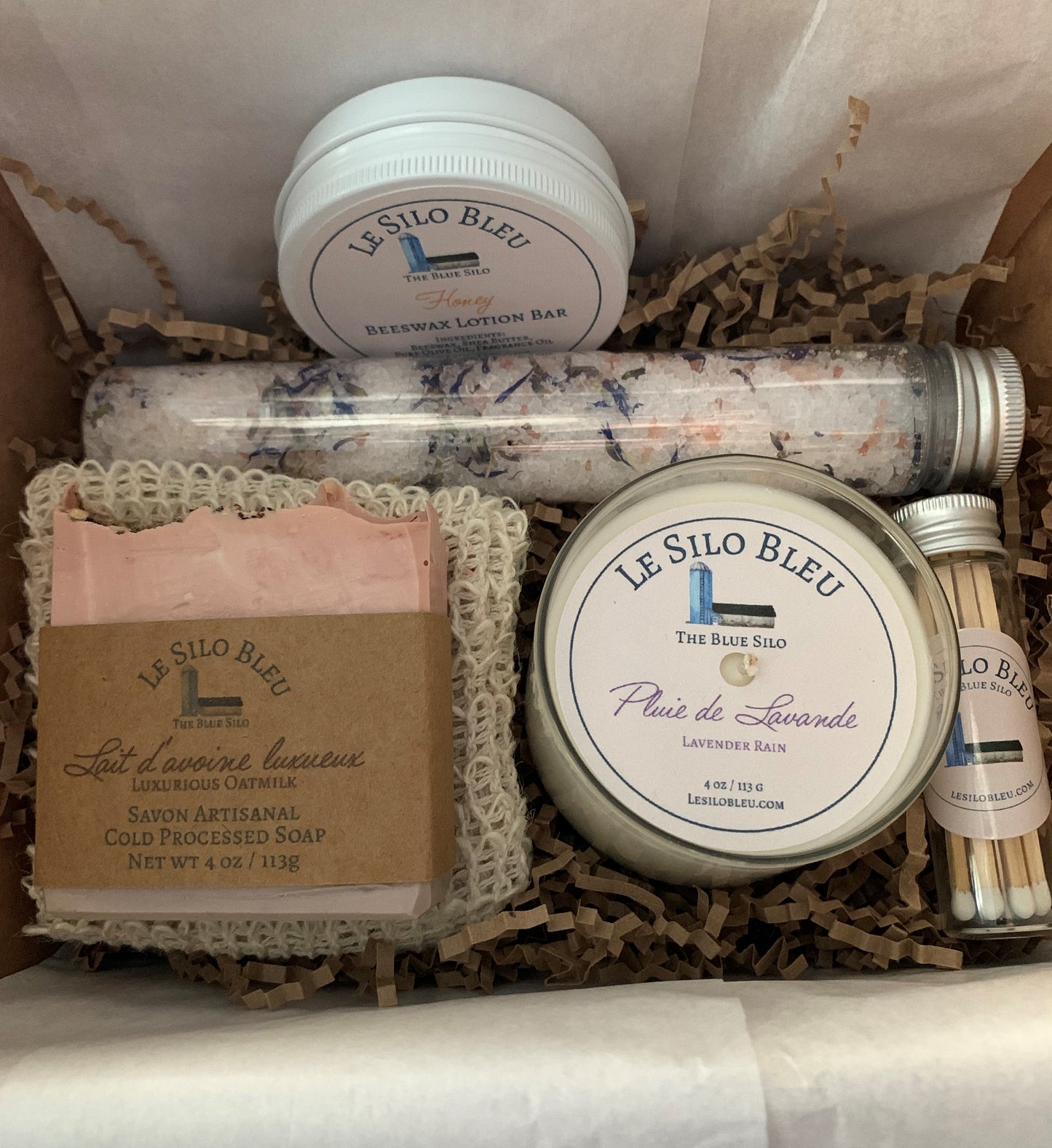 Pamper Yourself Gift Box - Includes Lotion Bar, One Bar Cold Processed Soap with Soap Saver Exfoliating Bag, Small 4 ounce candle, Bath Salts and Matches. This box is open and shows the contents nestled in natural brown crinkle paper with white tissue paper that will be folded over it once it's packed in the natural box with natural ribbons and tied in a bow.