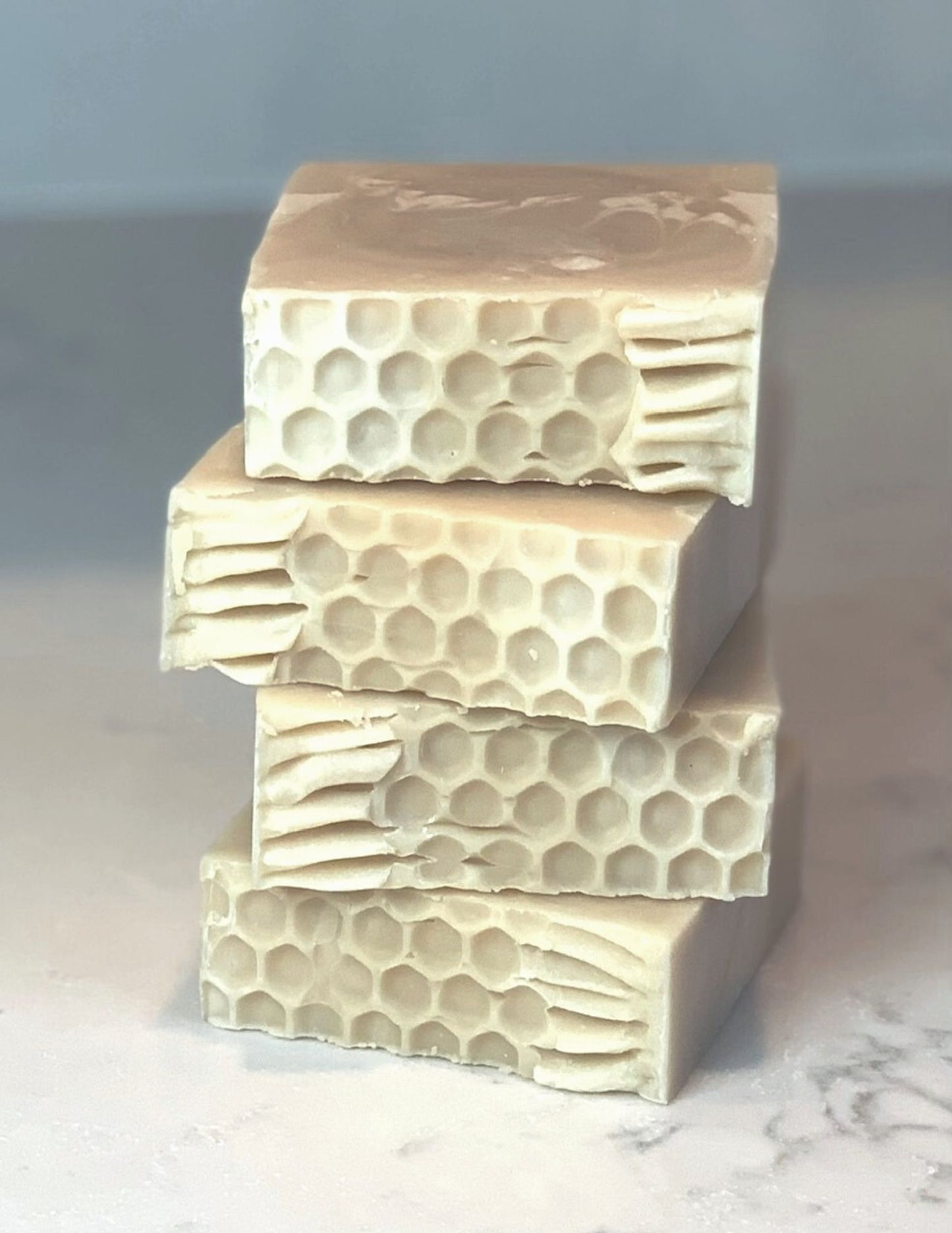 Stack of four triple butter honey soaps detailing honeycomb design on top. All soap is sitting on a marble counter with white background.
