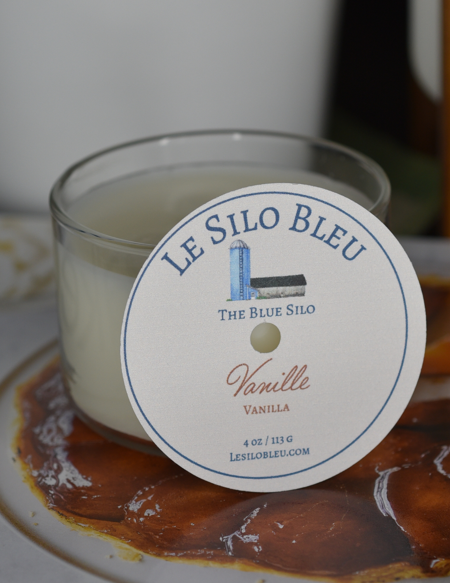 A vanilla scented candle is sitting on top of a French magazine with a plant in a white pot in the background.