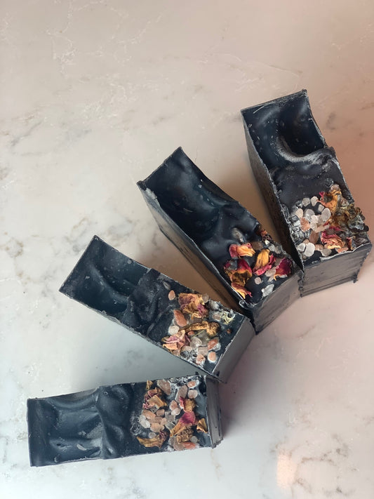 This beautiful deep black soap with pink and red rose petals and pink sea salt are sprialed on a marble table and a top down view.