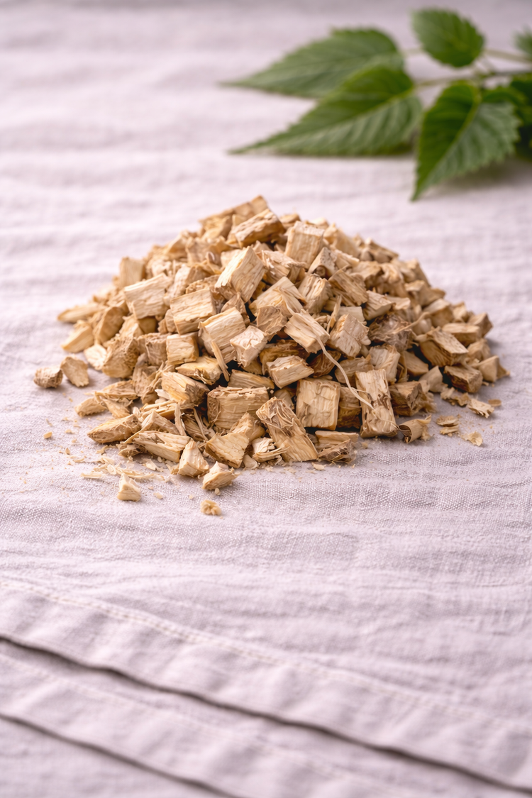 Dried pieces of marshmallow root on a linen tablecloth with a plant in the background.