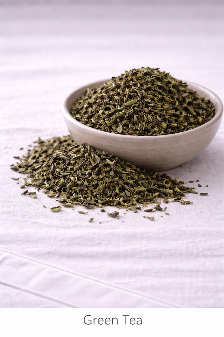 Dried green tea leaves in a rustic bowl with more leaves around it sitting on a linen tablecloth.
