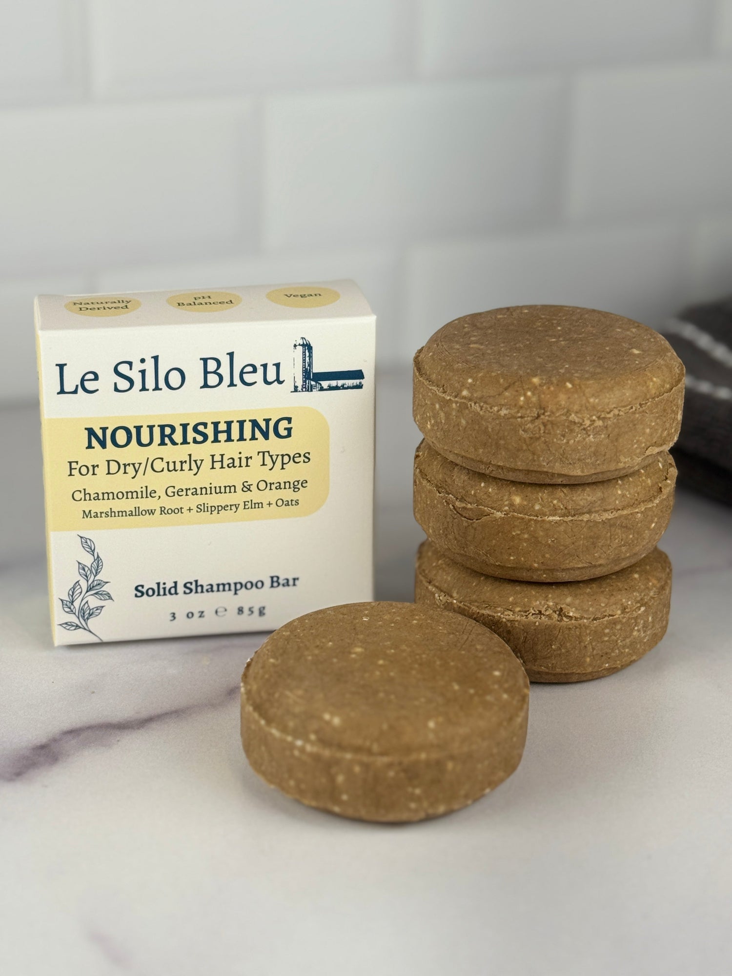 A stack of three and one single solid nourishing shampoo bar on a marble surface with a white tile background. These yellow orange bars are for dry and curly hair types.