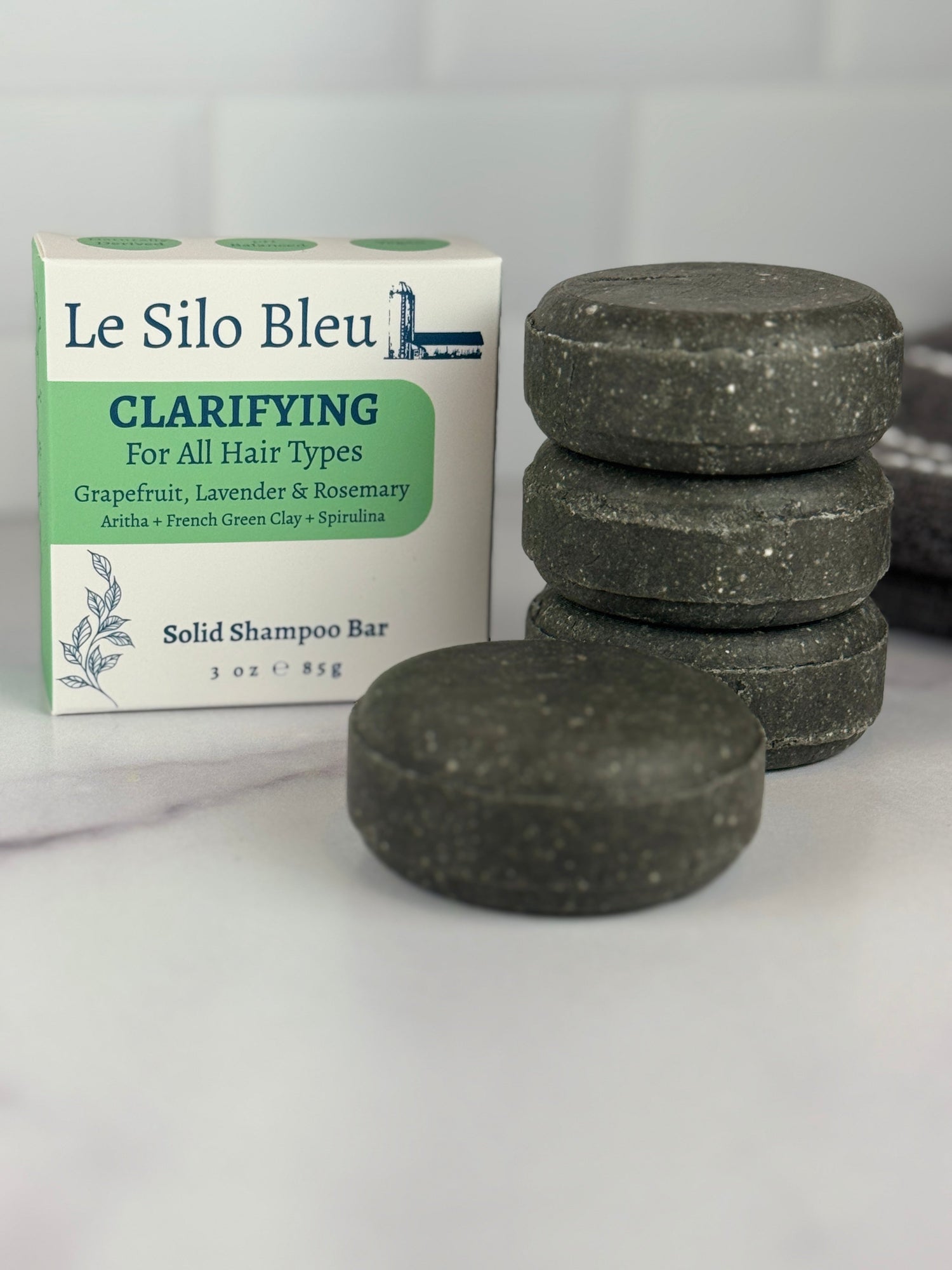 A stack of three and a single Clarifying shampoo bar sitting on a marble table with a white tile backsplash in the background.