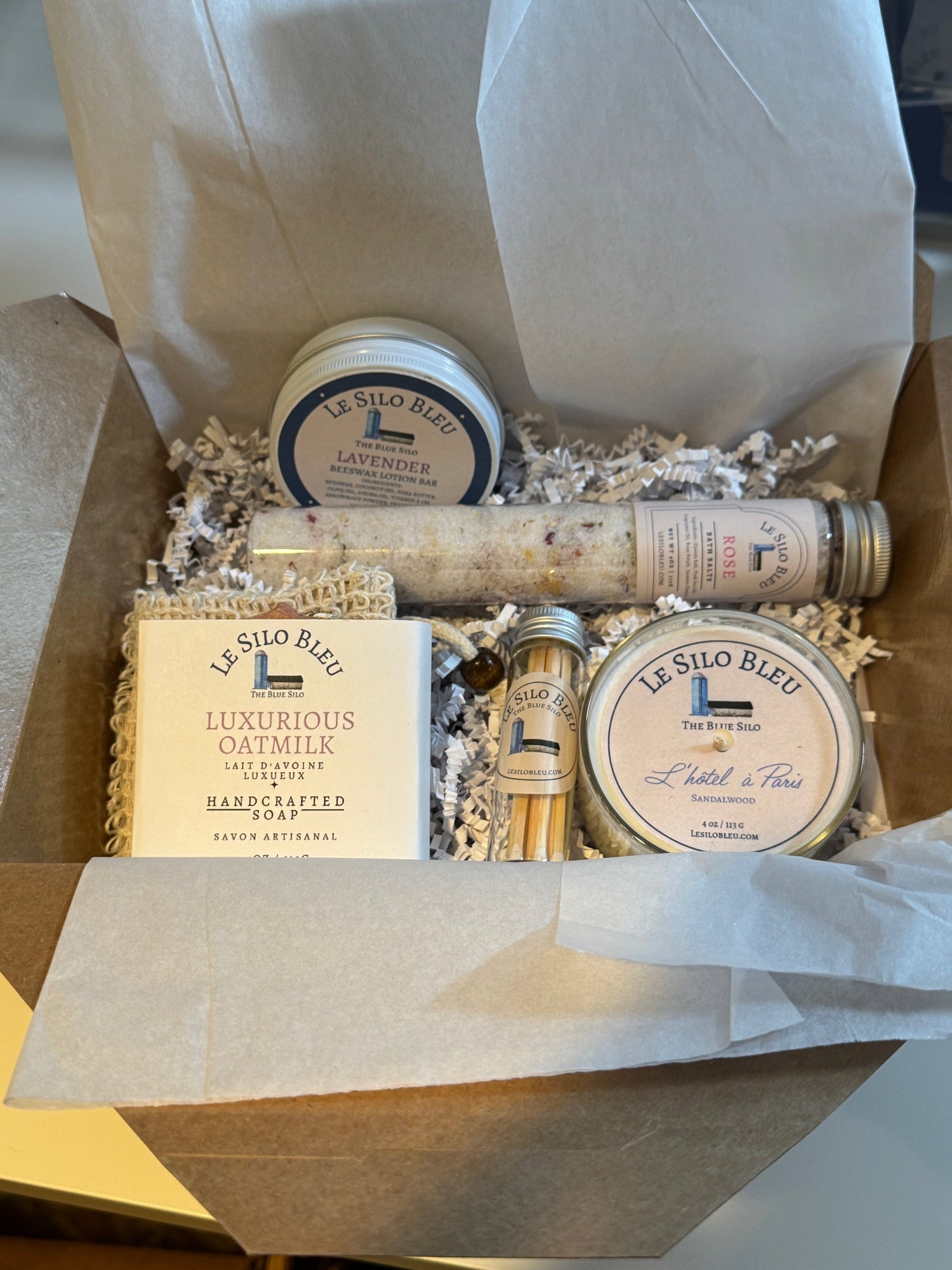Set of Silo Bleu products- small candle with matches, bar of soap with sisal bag, bath salts tube and a lotion bar in a brown paper box with white tissue paper.