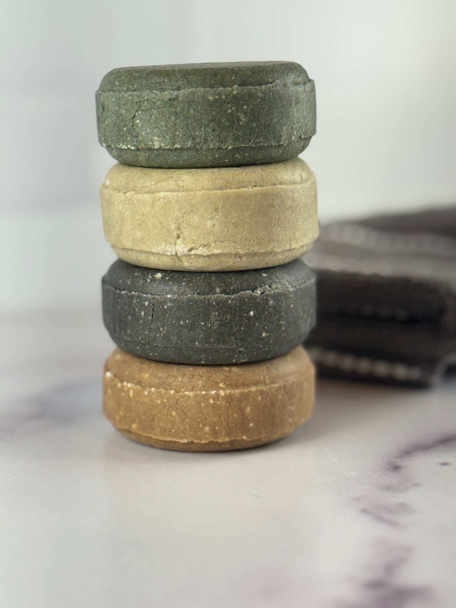 Stack of four shampoo bars on a marble surface with a white background and a grey towel on the surface