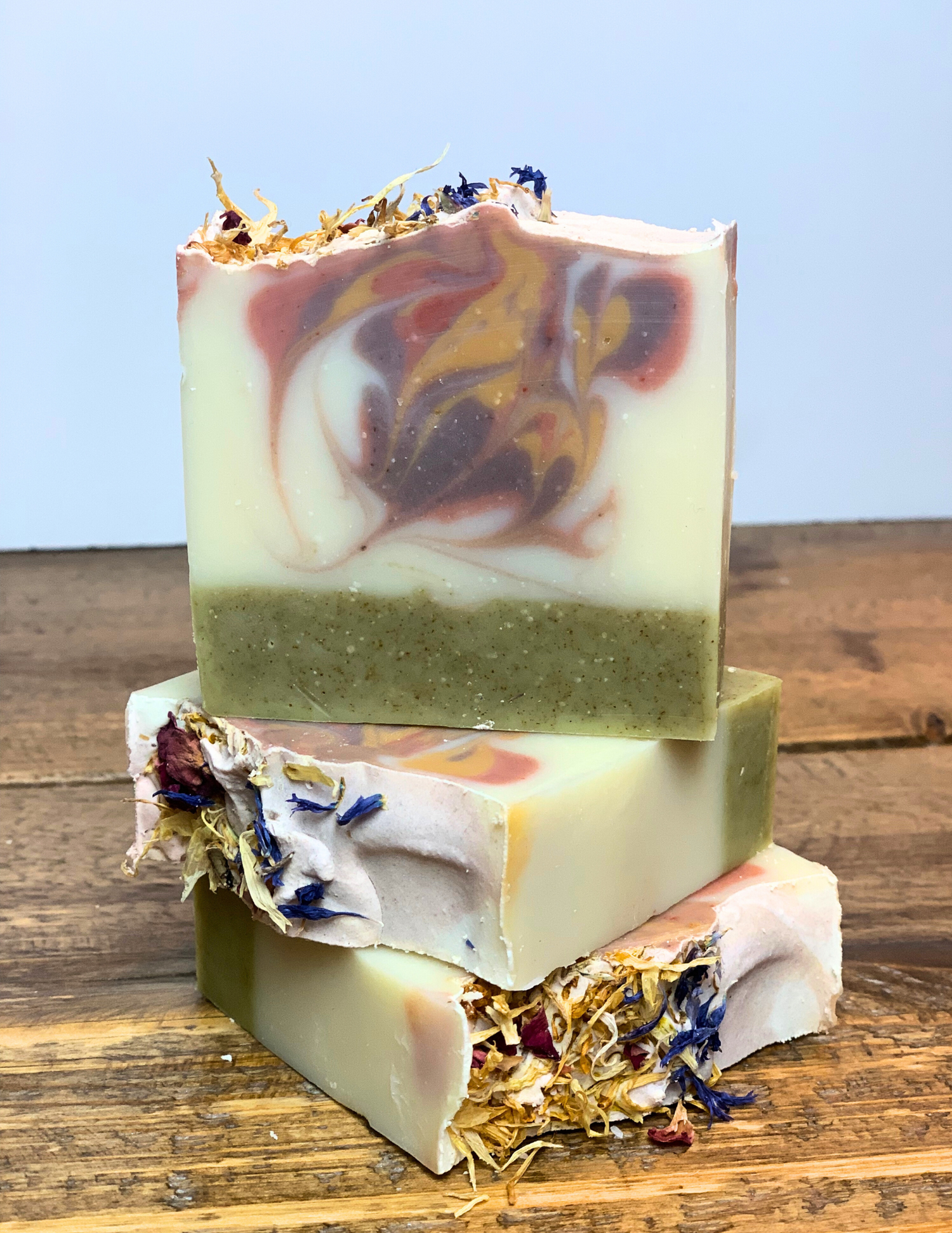 Stack of three Spring Meadow soaps sitting on a wood tabletop with floral botanical petals on top.