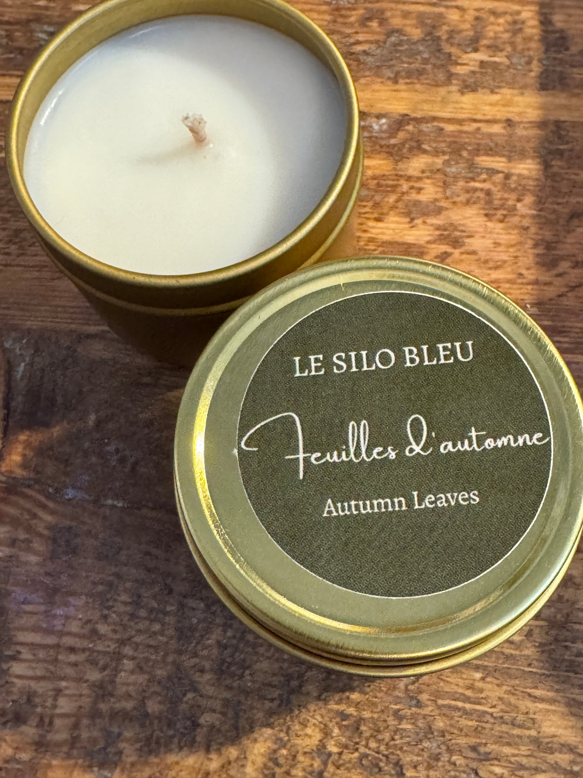 Candle in a gold tin with 'Le Sulo Bleu' label on a wooden surface