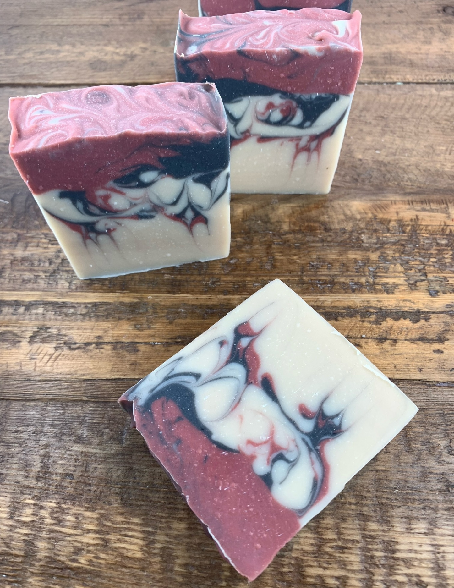 Three bars of Black Raspberry Vanilla soaps sit on top of a wooden table. Swirls of dark pink and black run through the soap.