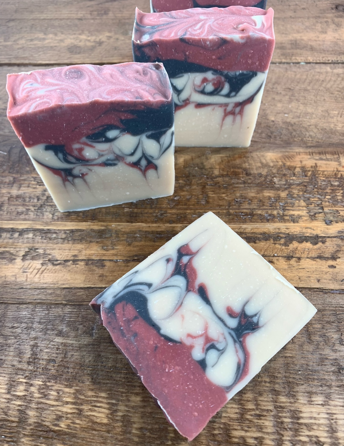Black raspberry scented soap bars with pink and black swirls of color throughout laying on a wooden table. 