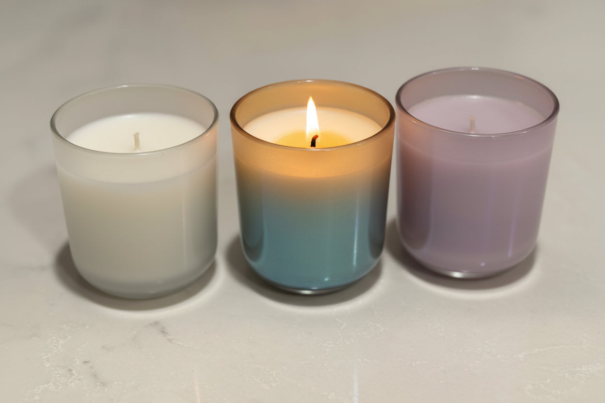 Three glass candles with different color gradients on a white surface.