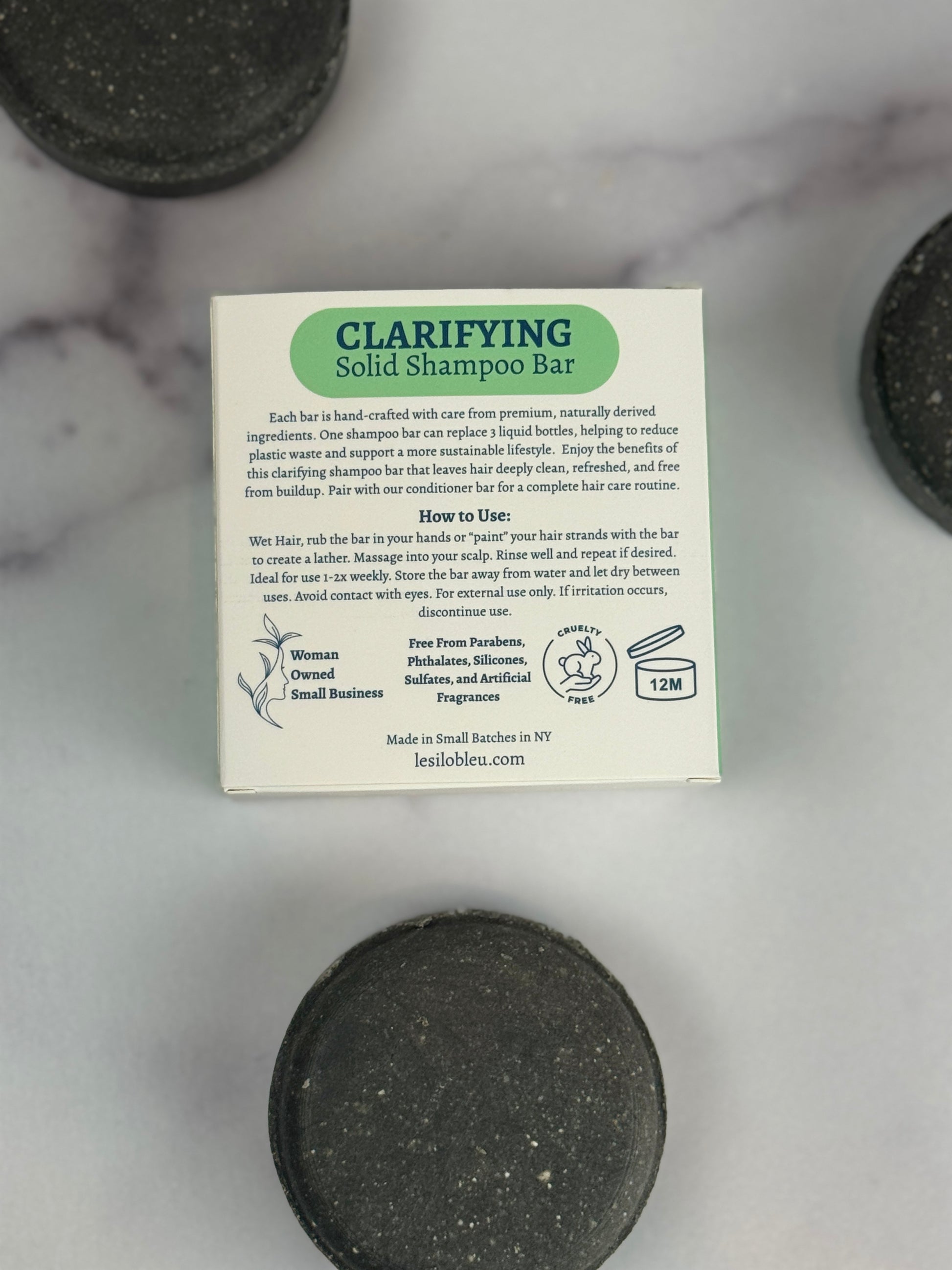 Clarifying solid shampoo bar with back packaging label on a marble surface with three partial bars laid out.