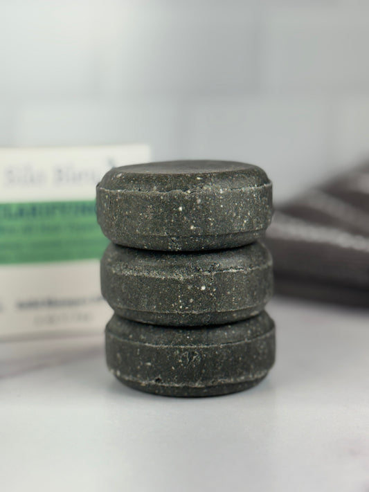 Stack of  three Clarifying Solid Shampoo  bars on a white surface with a white surface with a blurred background