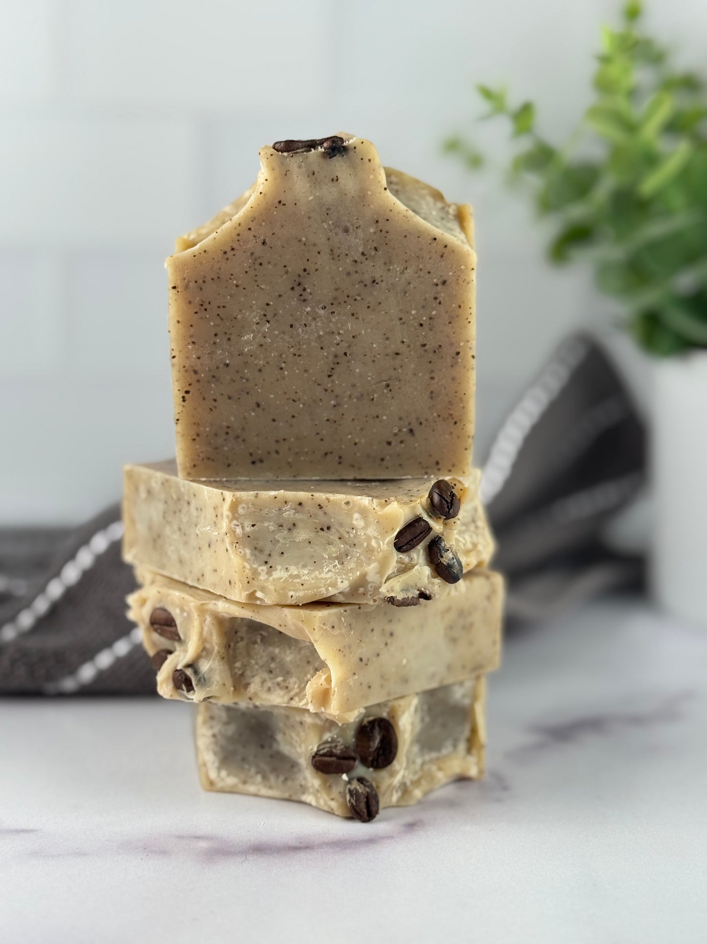 Stack of three soap bars with visible coffee beans on a marble surface.