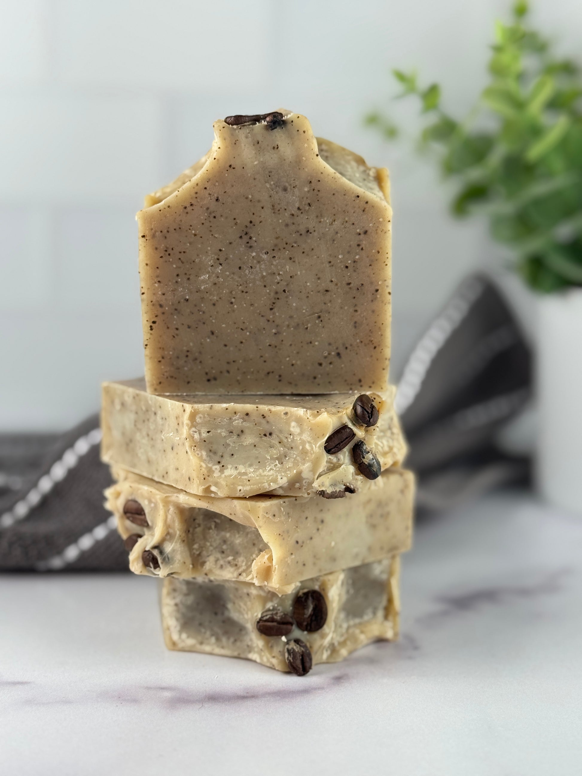 Stack of three soap bars with visible coffee beans on a marble surface.