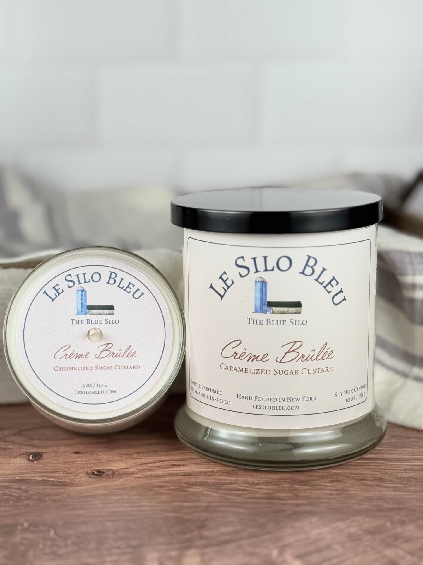 Two scented soy wax candles in jars, with the label 'LE SILON BLEU' and 'CÉme Brülée Caramelized Sugar Custard'. The larger jar is placed in front, and the smaller one is placed behind it.