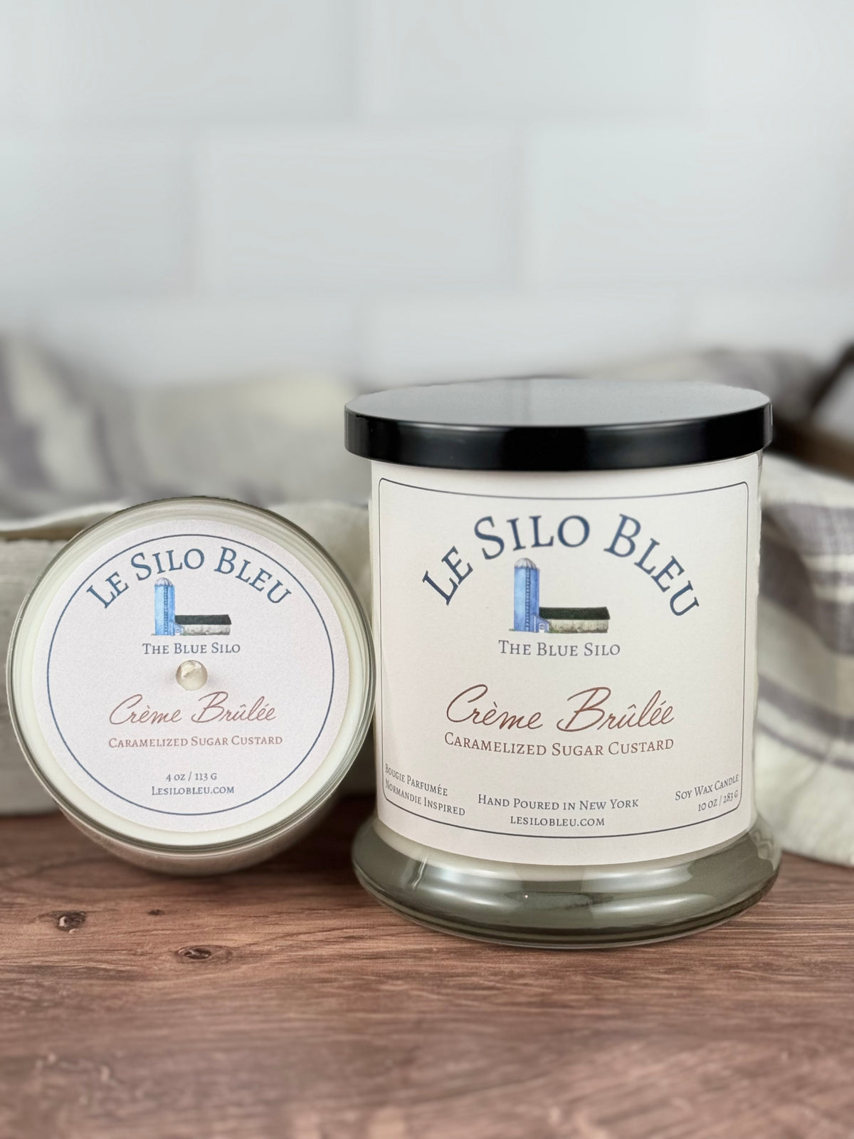 Two scented soy wax candles in jars, with the label 'LE SILON BLEU' and 'CÉme Brülée Caramelized Sugar Custard'. The larger jar is placed in front, and the smaller one is placed behind it.