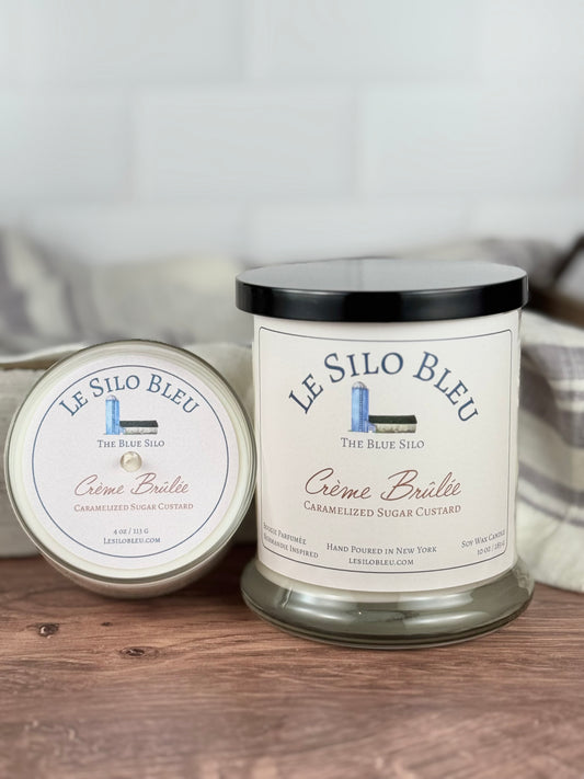 Two scented soy wax candles in jars, with the label 'LE SILON BLEU' and 'CÉme Brülée Caramelized Sugar Custard'. The larger jar is placed in front, and the smaller one is placed behind it.