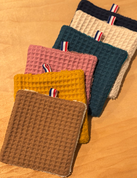 Five textured fabric cosmetic cotton pads in different colors on a wooden surface