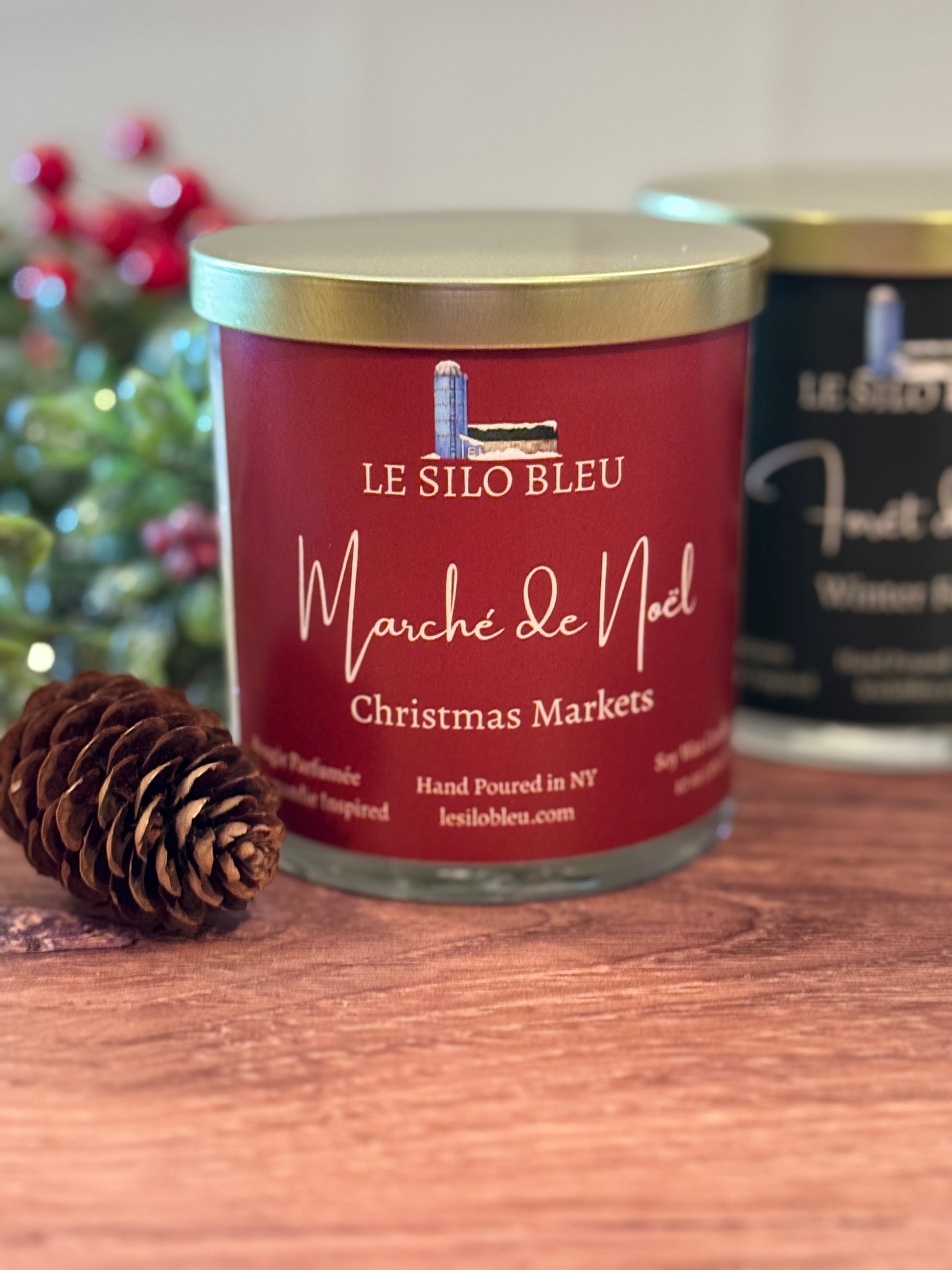 Red candle jar with gold lid labeled 'Le Silo Bleu Marché de Noel Christmas Markets' on a wooden surface.