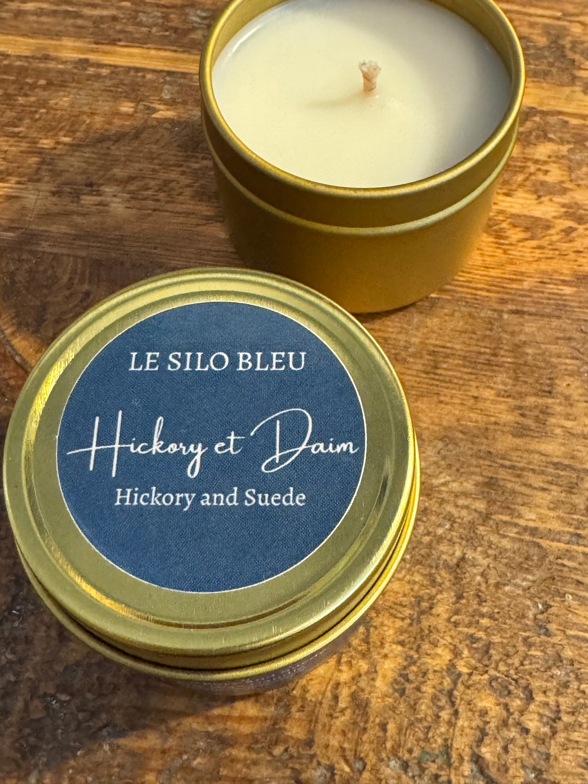 Candle in a gold tin with a blue label on a wooden surface