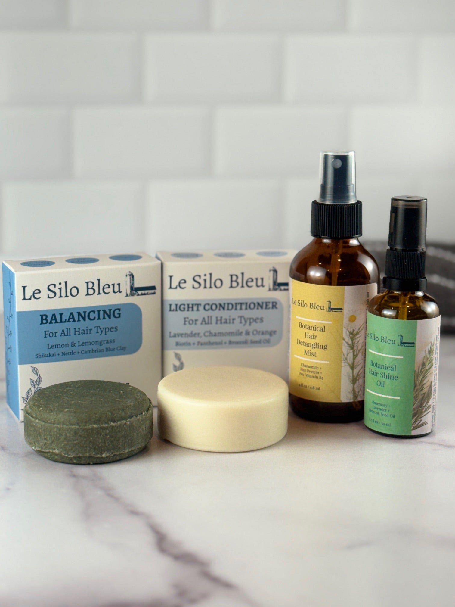 Collection of Le Silo Bleu hair care products on a marble surface with a tiled wall background.