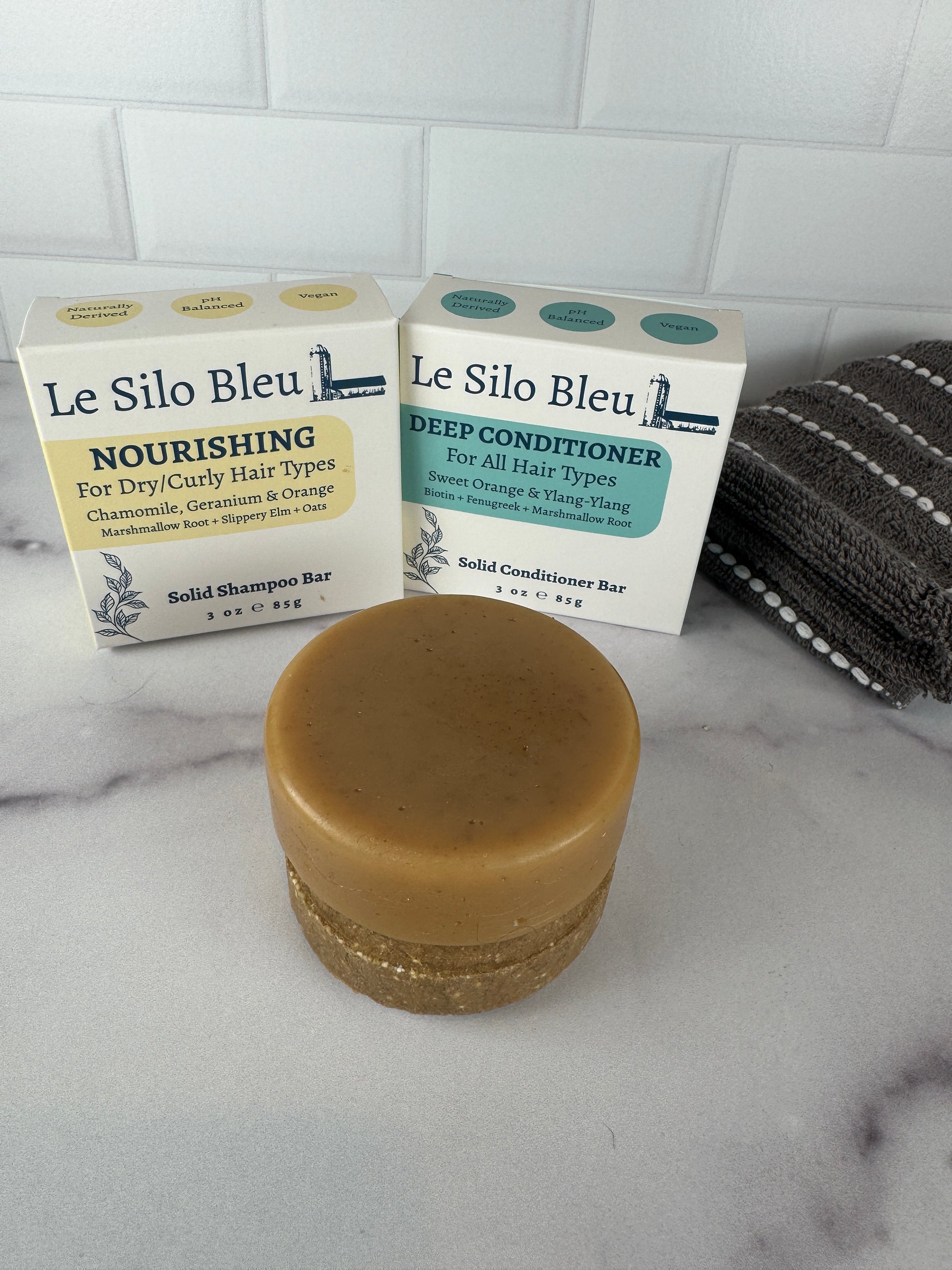 Bar of solid conditioner stacked on top of a solid shampoo bar and boxes labeled 'Le Silo Bleu' on a marble surface