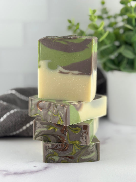 Stack of three green and cream marbled soap bars on a white surface with a plant in the background