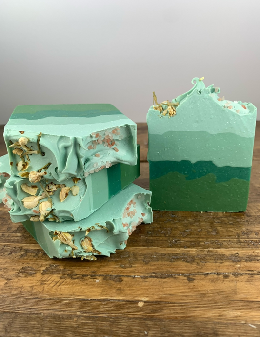 Soft Eucalyptus Soap on a wooden table. Ombre green soap with several layers of green and topped with pink sea salt and dried jasmine fiowers