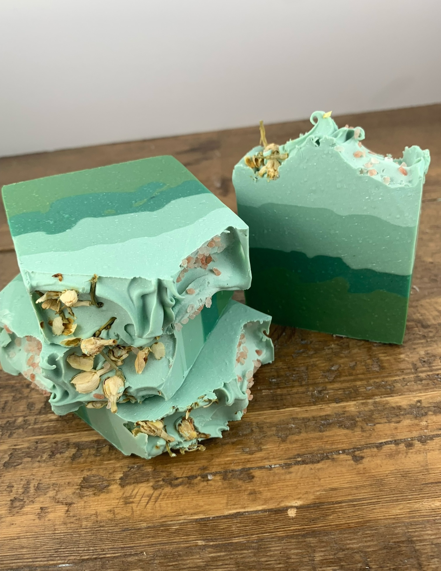 Soft Eucalyptus Soap on a wooden table. Ombre green soap with several layers of green and topped with pink sea salt and dried jasmine fiowers