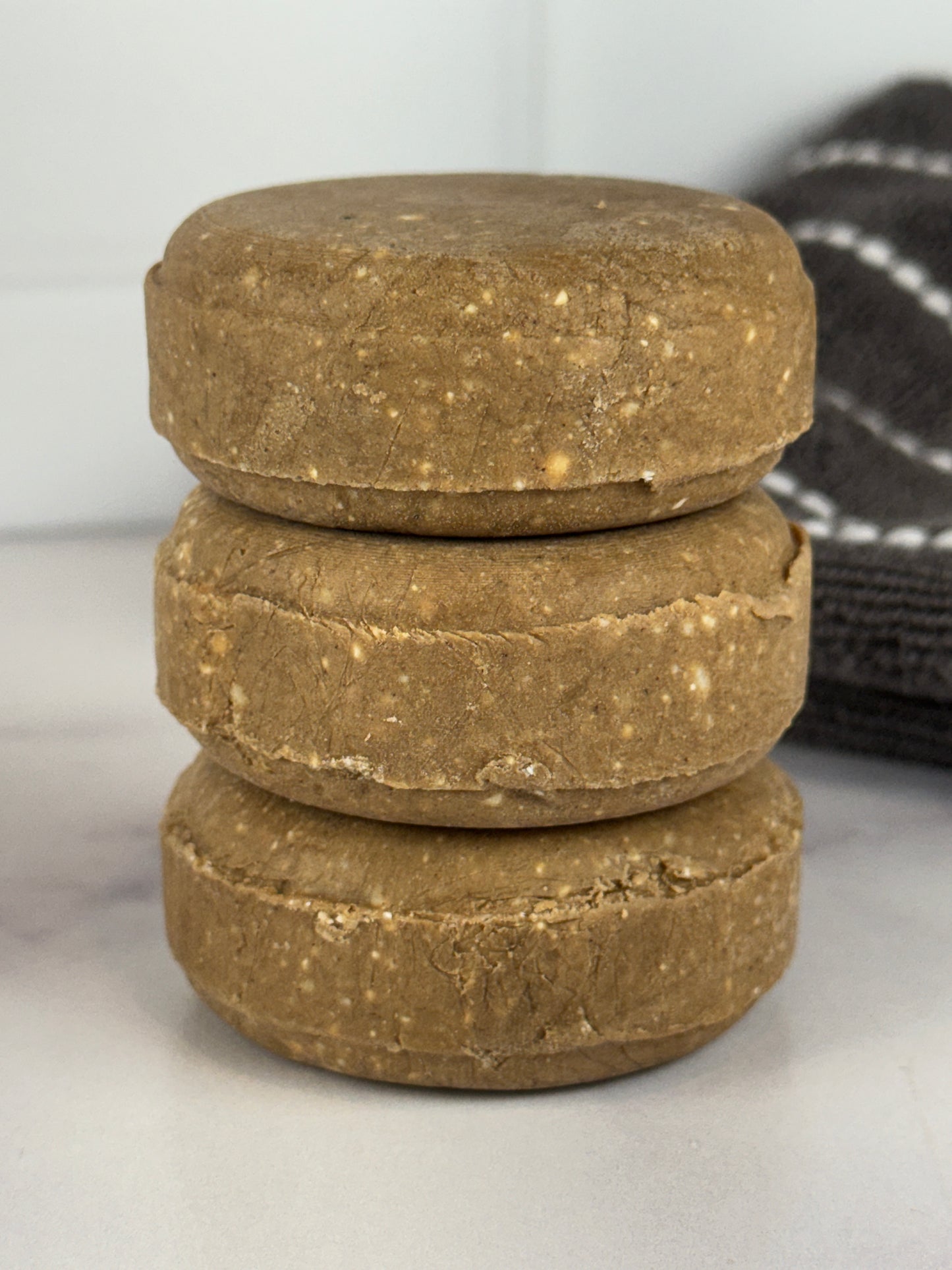 Stack of Nourishing Solid Shampoo bars on a white surface with a black and white striped towel in the background.