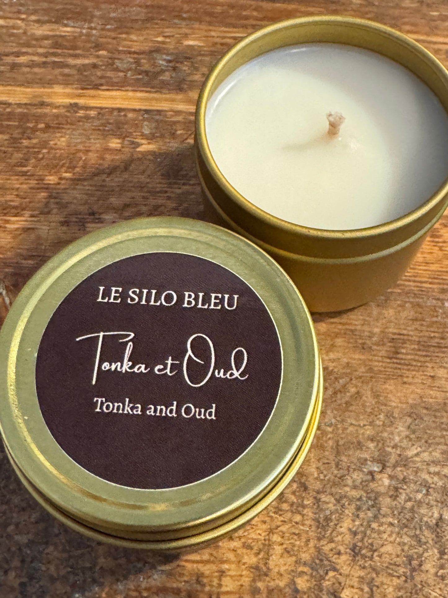 Candle in a brass tin with a label on a wooden surface